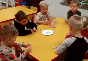 Kilkoro dzieci przy stoliku nawleka kolorowe koraliki na kreatywne druciki.