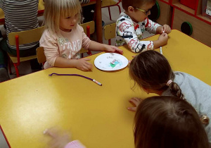 Kilkoro dzieci przy stoliku nawleka kolorowe koraliki na kreatywne druciki.
