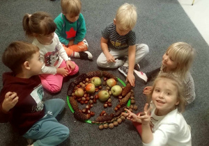 Kilkoro dzieci współpracując w grupie ułożyło w obręczy jesienną mandalę.