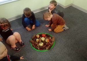 Kilkoro dzieci współpracując w grupie ułożyło w obręczy jesienną mandalę.