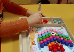 Chłopiec układa obrazek za pomocą drewnianej pęsety i kolorowych kulek.