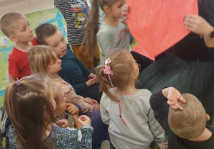 Ciocia Ola z Miejskiej Biblioteki Publicznej w Ozorkowie prezentuje dzieciom z grupy Biedronek zabawę andrzejkową, polegająca na przebijaniu wielkiego, czerwonego serca, na odwrocie którego są zapisane różne imiona.