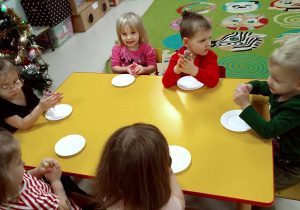 Kilkoro dzieci siedzi przy stole i rozgrzewa w dłoniach kolorowy lukier w tubkach.