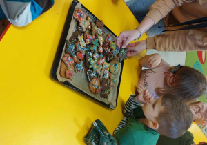 Kilkoro dzieci przy stoliku ogląda własnoręcznie ozdobione pierniczki.