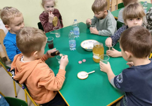 Kilkoro dzieci przy stoliku w trakcie przygotowania zdrowych, kolorowych napojów.