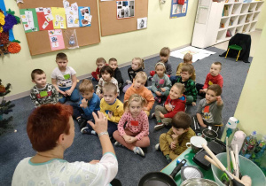 Wizyta pani kucharki z przedszkolnej kuchni - p. Barbary Skonieczko. Dzieci siedzą na dywanie i uważnie słuchają.