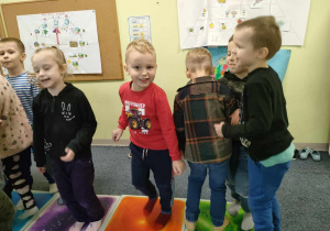 Kilkoro dzieci z grupy "Pszczółek" w trakcie zabawy na kolorowych płytkach sensorycznych.