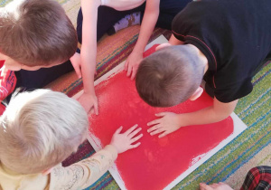 Kilkoro dzieci z grupy "Skrzatów" dotyka rączkami czerwonej płytki sensorycznej.
