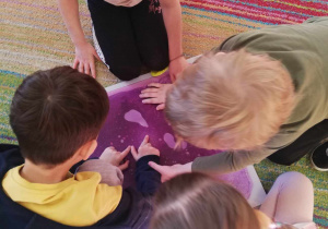 Kilkoro dzieci z grupy "Skrzatów" dotyka rączkami fioletowej płytki sensorycznej.