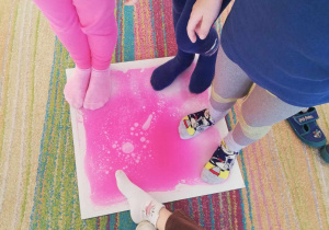 Kilkoro dzieci z grupy "Skrzatów" dotyka stopami różowej płytki sensorycznej.