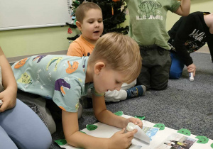 Arturek przyczepia ilustrację dziecka na hulajnodze na kartkę z dobrymi praktykami dla środowiska.