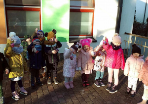 Dzieci z grupy "Motylków" ciepło ubrane wraz ze swoimi lodowymi ozdobami na tarasie przedszkolnym.