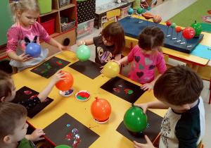 Kilkoro dzieci przy stole podczas malowania balonami.