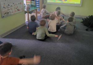 Dzieci siedzą przed tablicą interaktywną i biorą udział w ćwiczeniach wyciszających.