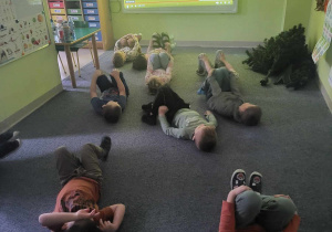 Dzieci siedzą przed tablicą interaktywną i biorą udział w ćwiczeniach wyciszających i rozciągających.
