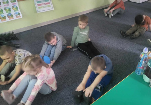 Dzieci siedzą przed tablicą interaktywną i biorą udział w ćwiczeniach wyciszających i rozciągających.