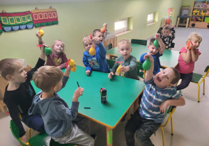Dzieci siedzą przy stole i prezentują swoje gniotki.
