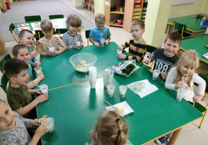 Degustacja "Koktajlu Shreka" w naszej grupie. Dzieci siedzą przy połączonych stołach i chętnie próbują nowych smaków.