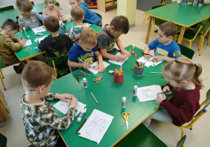 Kilkoro dzieci przy stole starannie koloruje naklejony w całości wybrany przez siebie szablon.