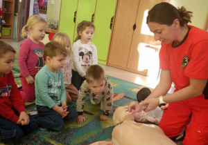 Pani Kamilka prezentuje dzieciom profesjonalne uciskanie klatki piersiowej na fantomie.