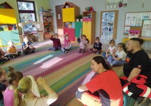 Dzieci z grupy "Skrzatów" siedzą na dywanie podczas pogadanki z ratownikami medycznymi.