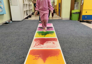 Zuzia idzie stopa na stopą po kolorowej ścieżce sensorycznej.