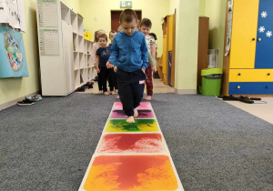 Szymon idzie stopa na stopą po kolorowej ścieżce sensorycznej.
