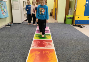 Filip idzie stopa na stopą po kolorowej ścieżce sensorycznej.