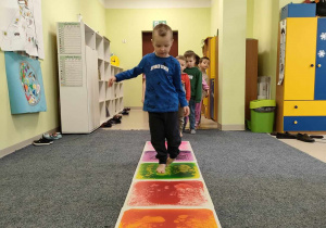 Adam idzie stopa na stopą po kolorowej ścieżce sensorycznej.