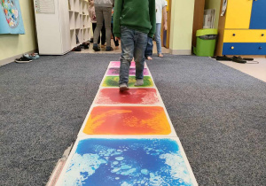 Kornel idzie stopa na stopą po kolorowej ścieżce sensorycznej.