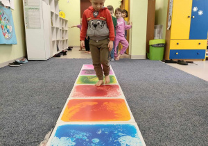 Igor idzie stopa na stopą po kolorowej ścieżce sensorycznej.