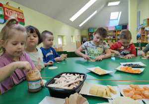 Przygotowanie "Misiowych słodkości". Dzieci smarują masłem orzechowym swojego wafelka.