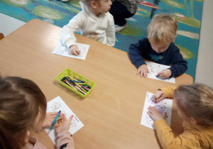 Kilkoro dzieci z grup młodszych koloruje szablon trzech małych świnek przy stole.