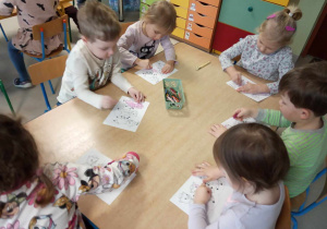 Kilkoro dzieci z grup młodszych koloruje szablon trzech małych świnek przy stole.