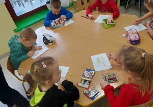 Kilkoro dzieci z grupy "Biedronek" przy stole koloruje szablon bajki "Brzydkie kaczątko".