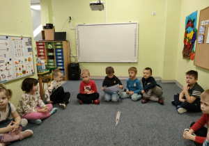 Dzieci z grupy "Pszczółek" siedzą w kolę i po kolei oglądają ilustrację do bajki, jednocześnie słuchając jej treści.