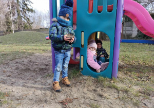 Kornel, Zuzia i Kajtek przy konstrukcji na przedszkolnym placu zabaw.