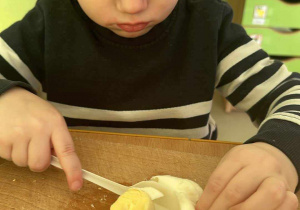 Przygotowanie sałatki brokułowej - Stefcio kroi jajko na małe kawałeczki za pomocą plastikowego noża.
