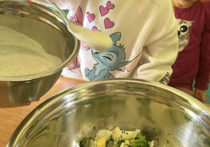 Przygotowanie sałatki brokułowej - Jagódka za pomocą łyżki dodaje do sałatki jogurt naturalny.