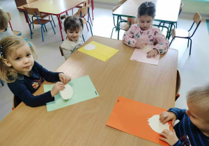 Kilkoro dzieci przy stoliku wykonuje pracę plastyczną - cebulka z kolorowego papieru.