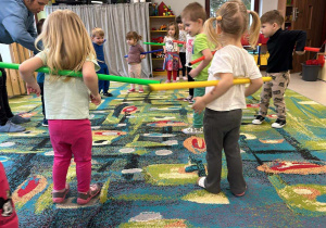 Maluszki stoją na dywanie i trzymają kolorowe laski gimnastyczne.