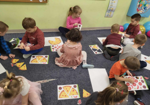 Dzieci z grup: "Pszczółek" i "Biedronek" siedzą na dywanie i wypychają gotowe elementy, by stworzyć ulubioną pizzę.