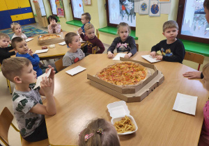 "Biedronki" siedzą przy stole i będą jeść pyszną pizzę, dostarczoną z Pizzerii "Źródełko".