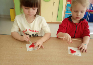 Kornelka i Helenka z "Żabek" malują serduszka za pomocą czerwonej farby oraz pędzelka.