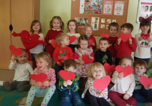 Dzieci z najmłodszej grupy pozują do pamiątkowego, walentynkowego zdjęcia z szablonami czerwonych serduszek.