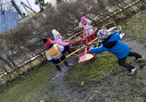 Antoś kręci kolegę i koleżanki na karuzeli na przedszkolnym placu zabaw.