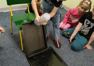 Kajtuś uczestniczy w eksperymencie - "wodna ścianka". Pozostałe dzieci siedzą w kole i obserwują.