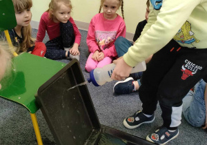 Leoś uczestniczy w eksperymencie - "wodna ścianka". Pozostałe dzieci siedzą w kole i obserwują.