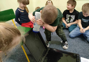 Antoś uczestniczy w eksperymencie - "wodna ścianka". Pozostałe dzieci siedzą w kole i obserwują.