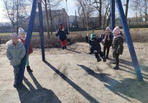 Kilkoro dzieci z grup: "Skrzatów" i "Biedronek" na huśtawkach na placu zabaw w Parku Miejskim.
